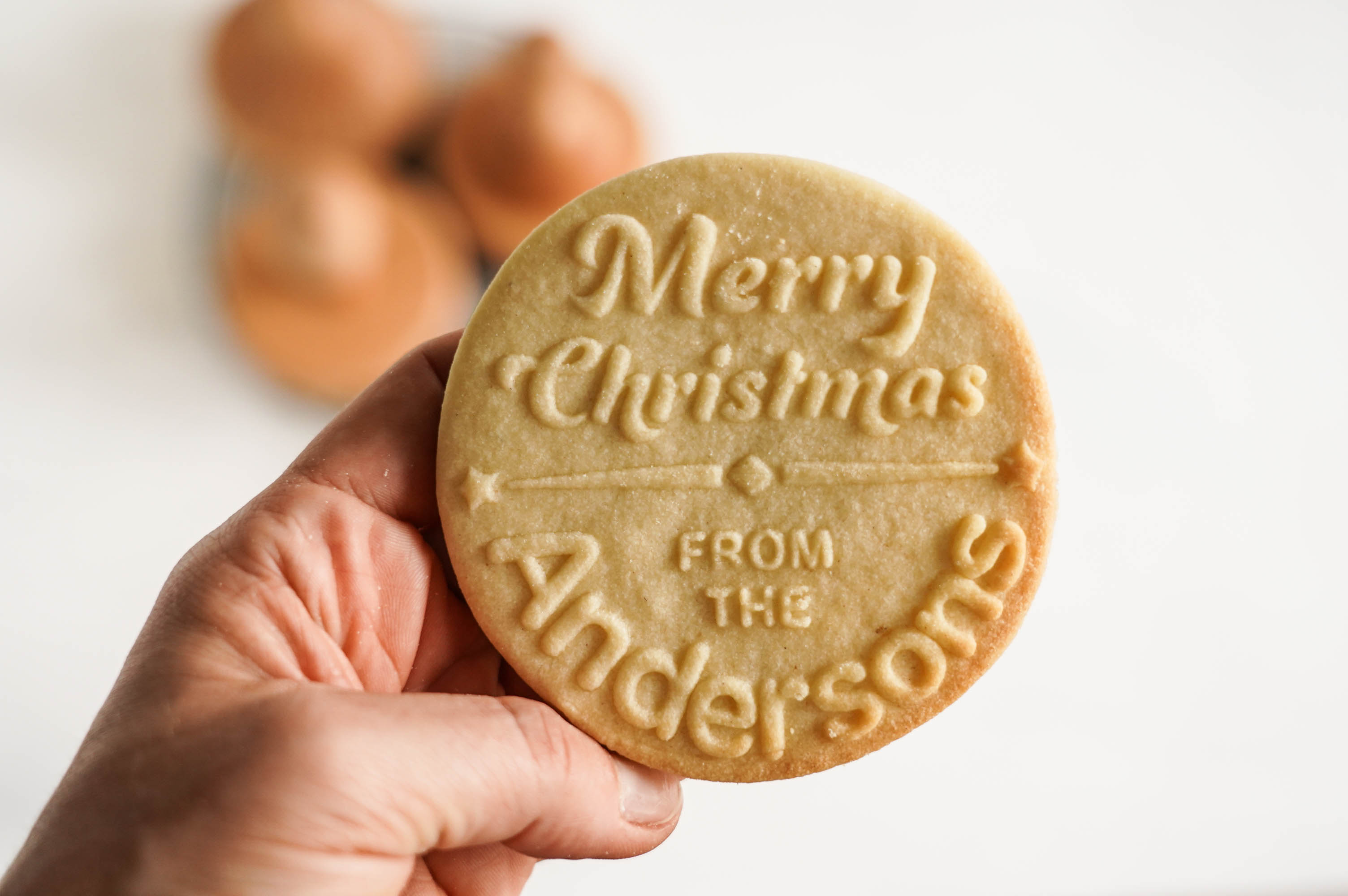 Dłoń trzyma duże ciastko z wytłoczonym wzorem Merry Christmas from the Andersons